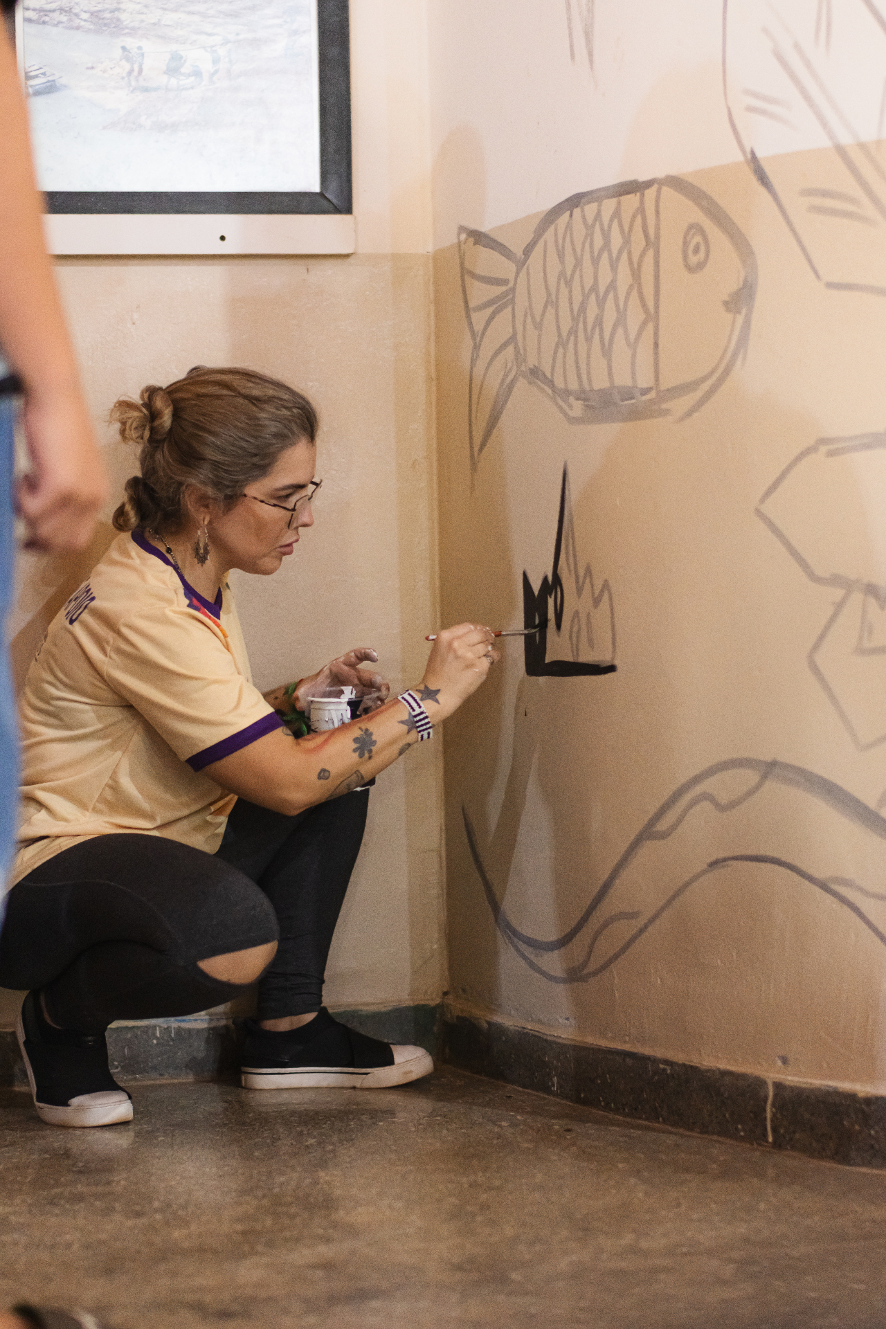 Artista pintando detalhes de um mural com peixes durante oficina cultural